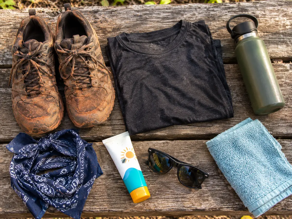 Mit roter Erde verschmutzte Sneaker, ein dunkles T-Shirt, eine Wasserflasche, ein Bandana und ein Handtuch auf einer Bank